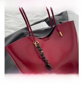 Close-up of deep red glossy tote bag featuring gold hardware and a braided strap detail