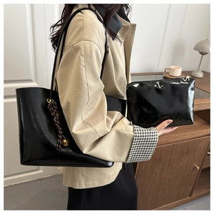 Detail of black glossy tote bag with gold charm and matching pouch on model