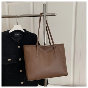 Detail of dark brown leather tote bag hanging on a rack with a tweed jacket