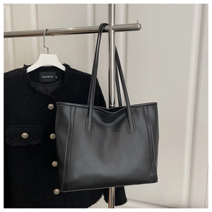 Detail of a large black matte leather tote bag paired with a tweed jacket on a hanger