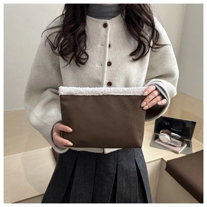 Detail of a dark brown PU clutch with white faux shearling trim held by a model
