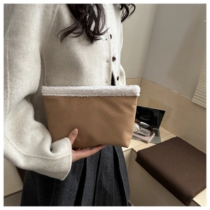 Dettaglio pochette in pelle marrone con bordo in agnello bianco tenuta da una modella