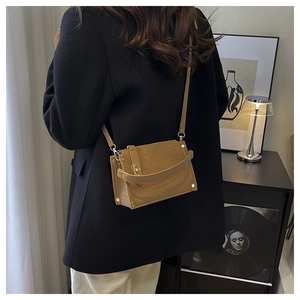 Détail d'un sac carré en cuir marron avec fermoir métallique porté par un mannequin