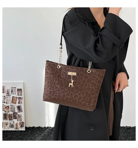 Detail of leopard print tote bag with gold chain strap and deer charm on black coat