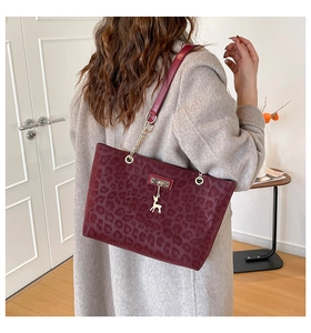 Detail of burgundy leopard print tote bag with golden deer charm and chain strap