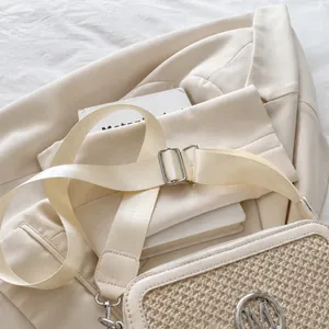 Detail der beigen gewebten Tasche mit silbernem M-Logo und breitem verstellbarem Schultergurt