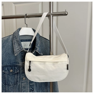 Detail der weißen Nylon-Halbmondtasche, die an einem Ständer mit Jeansjacke aufgehängt ist