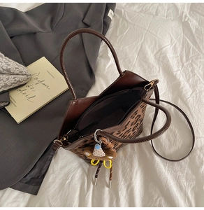 Detail of leopard print tote bag featuring brown leather handles and plush bear charm
