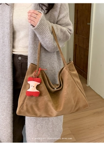 Detail of brown suede tote bag with minimalist shoulder straps and apple core charm