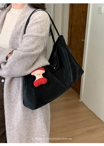 Detail of black tote bag featuring a cute red apple plush charm and matte texture finish