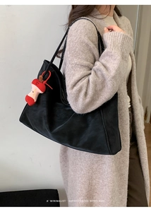 Detail of minimalist black suede tote bag with a distinctive red plush apple charm