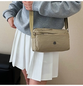 Detail showing the khaki nylon crossbody bag's multi-zipper layers and wide shoulder strap