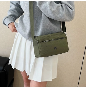 Close-up of olive green nylon crossbody bag with multiple zippers worn by a model