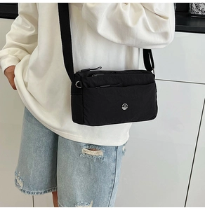 Close-up of a black nylon crossbody bag with metal M logo and double zip compartments