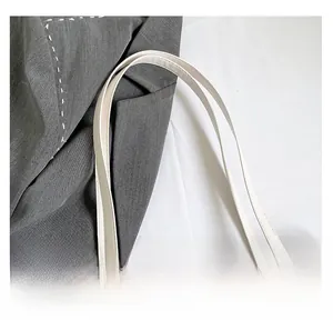 Detailed close-up of leather handle stitching and canvas texture on white tote bag