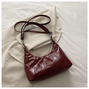Détail d'un sac hobo vintage bordeaux en cuir brillant sur un blazer crème