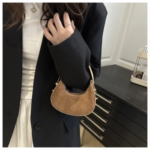 Detail van een bruine suède halve maan mini-tas vastgehouden in een minimalistische stijl