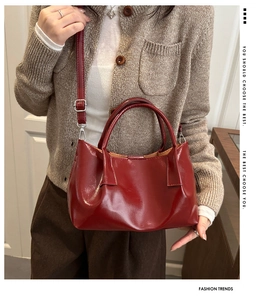 Close-up of a red pleated leather handbag worn cross-body on a brown knit sweater