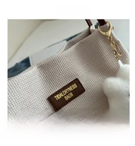 Détail du cabas tissé blanc cassé avec étiquette logo en cuir et charm nuage en peluche