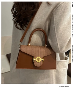 Dettaglio borsa a tracolla in pelle marrone con trama intrecciata e fibbia logo M dorata