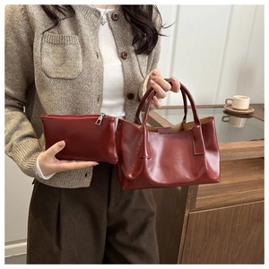 Detail of dark red vintage tote bag and matching pouch held by a model in warm light
