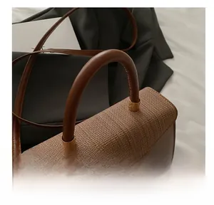 Dettaglio della trama intrecciata e della chiusura con logo dorato su borsa in pelle marrone