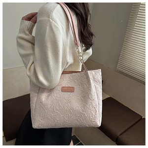 Détail d'un sac cabas beige avec tissu texturé, bandoulière chaîne et patch logo