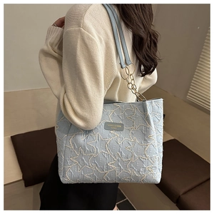 Détail d'un sac cabas bleu clair matelassé avec broderie et chaîne dorée