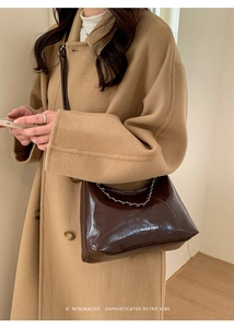 Dettaglio borsa sottobraccio marrone scuro lucida con catena su cappotto di lana