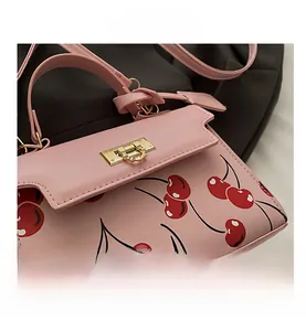 Detail view of pink handbag with red cherry print and golden metallic lock clasp