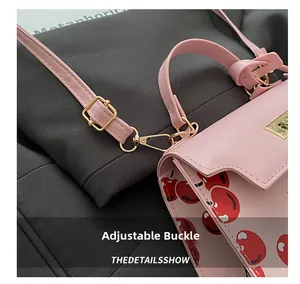 Detail view of pink leather bag with cherry print, gold hardware, and metal buckle