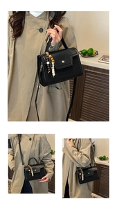 Detail van zwarte baguette tas met gouden gesp en accessoire met kralen hanger