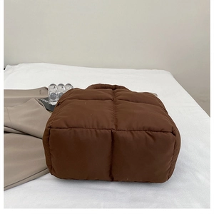Vista detallada del bolso acolchado marrón sobre tela blanca con accesorios de moda