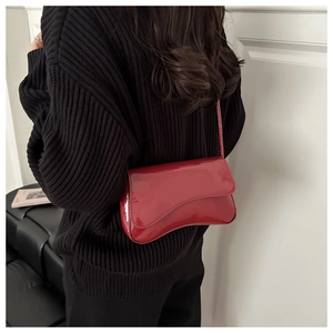 Detail of red patent leather shoulder bag with asymmetric flap shown on a model