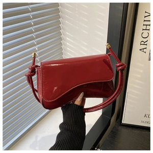 Detail of burgundy patent leather handbag featuring knot shoulder strap and flip cover