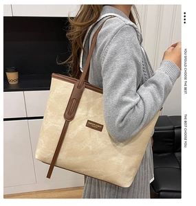 Detail of beige denim tote bag with brown leather handles worn by a model in casual setting
