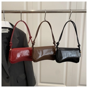Nahaufnahme dreier glänzender Lackleder-Schultertaschen in Burgund, Karamell und Schwarz