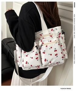 Detail of cherry print tote bag with multiple zipper pockets and white strap