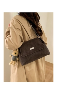 Détail d'un sac à bandoulière en daim marron foncé avec chaîne argentée et breloque