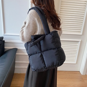 Bolso tote acolchado negro con correa ancha para el hombro en un entorno de interior