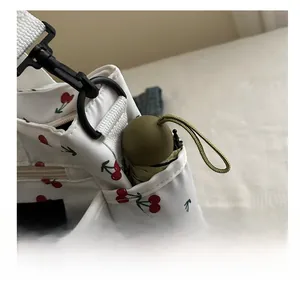 Detail view of white cherry print shoulder bag featuring a side pocket with a green umbrella