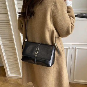 Retro black leather handbag with gold buckle shown worn with a wool coat