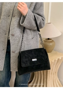 Détail d'un sac bandoulière en daim noir avec une chaîne argentée et boucle en métal