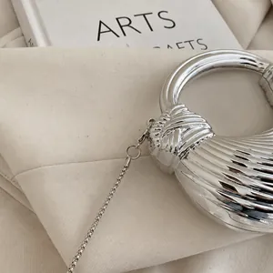 Detail der silbernen Wellen-Abendtasche mit rundem Metallgriff und Kettenelementen