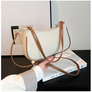 Detalle de bolso medialuna minimalista en tela beige con ribetes de cuero marrón y correa