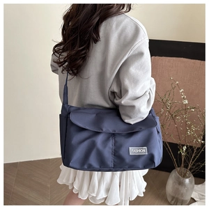 Detalle del bolso mensajero azul marino con etiqueta Fashion y cierre de solapa en modelo