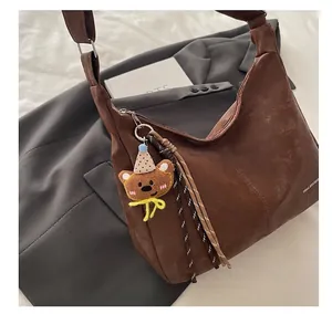 Gros plan du sac à bandoulière marron avec breloque ours et détails tissés