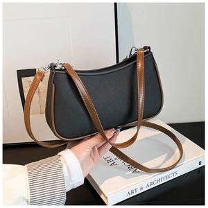 Detalle del bolso hobo de lona negra y piel marrón sostenido a mano con doble correa