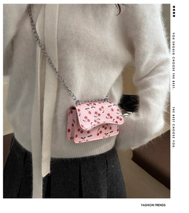 Detail of pink shoulder bag featuring cherry prints and silver chain strap on model