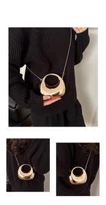 Detail view of a gold crescent-shaped mirror finish bag with a fine chain shoulder strap